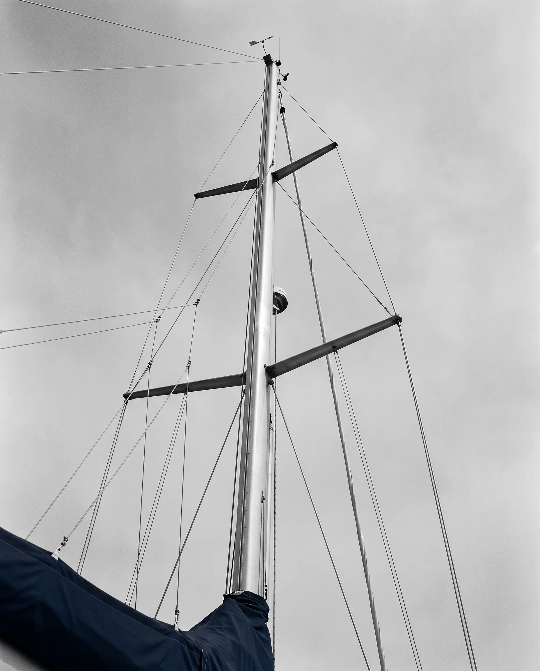 Looking up the mast of a moored sailing boat against an overcast sky.
