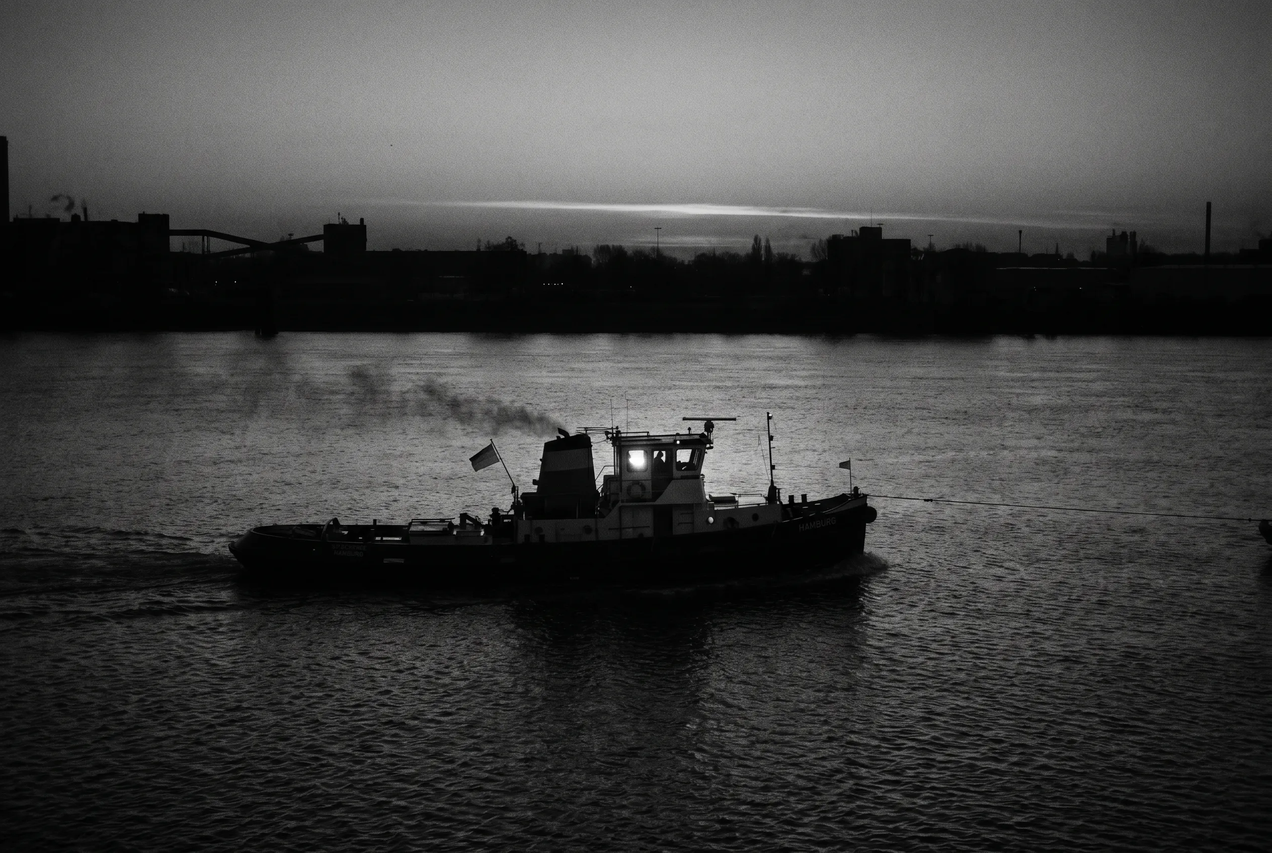 A small Hamburg-registered tugboat working the Elbe in low light.